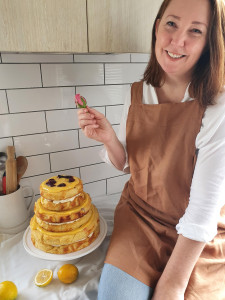 Rose Lawrence, Owner, wearing an apron and holding a flower next to a cake